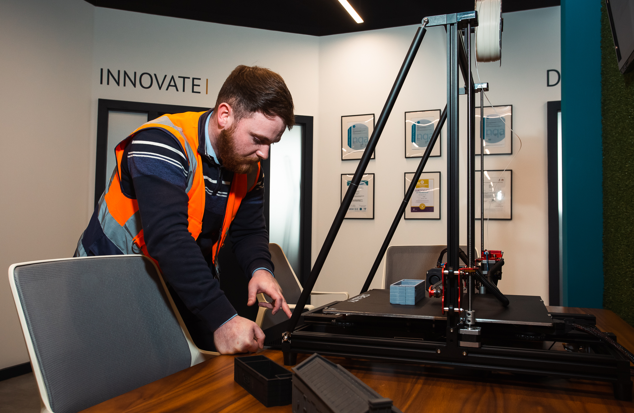 man in high vis at desk with 3d printer